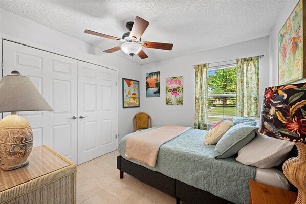 A bedroom with a bed, a ceiling fan, a lamp, and artwork on the walls.