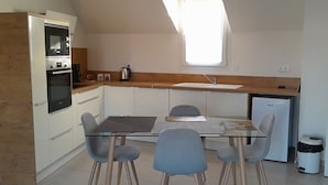 Een kleine keuken met een eettafel, stoelen, een koelkast en een magnetron.