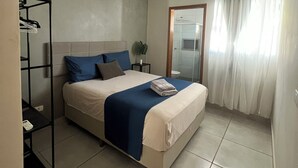 A neatly arranged bedroom with a bed, a bedside table, a mirror, and a window with curtains.
