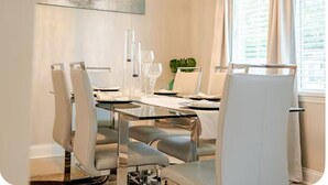 Een eetgedeelte met een glazen tafel, witte stoelen en een plant op tafel.