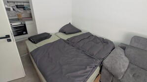 A small, compact bedroom with a single bed, a grey sofa, and a kitchenette area. - Small city apartment Remscheid (Remscheid)