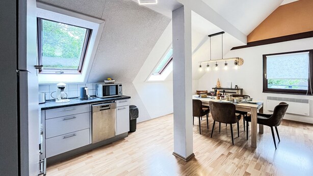 A modern kitchen with a dining area, featuring a skylight, wooden flooring, and contemporary appliances.