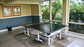 A ping pong table in a room with a view of greenery through large windows.