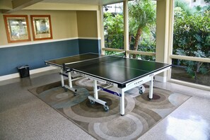 Mesa de ping pong en una habitación con vistas a la vegetación a través de amplias ventanas.