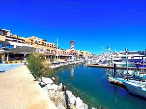 Un port de plaisance avec des bateaux amarrés, un ciel bleu et dégagé, et des bâtiments dotés de balcons.