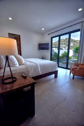Une chambre à coucher avec un lit, une lampe, une télécommande, une chaise et une vue sur l’extérieur.