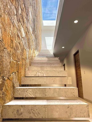 Un escalier avec un mur en pierre d’un côté et une lucarne au-dessus.