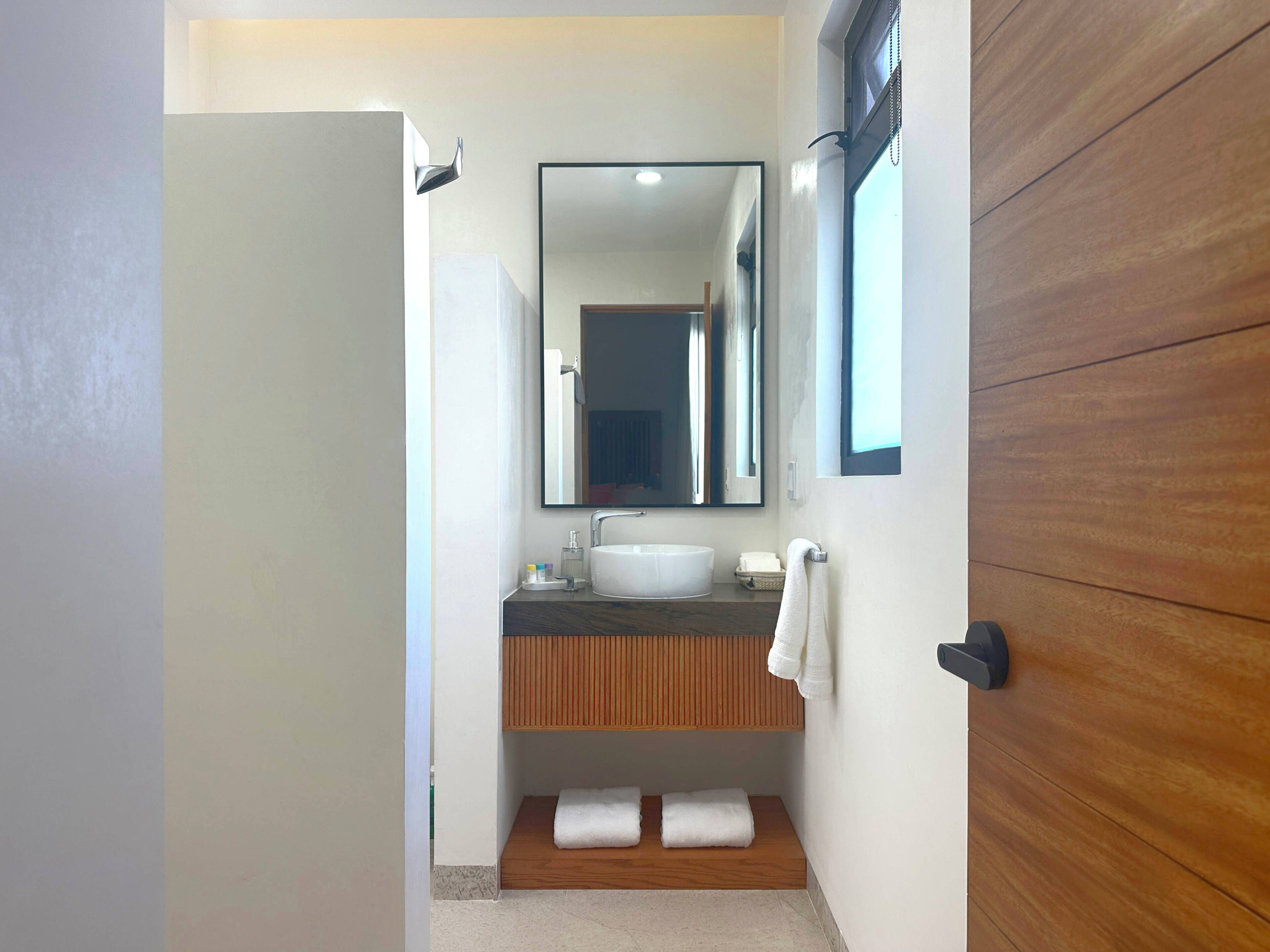 A modern bathroom with a wooden vanity, a large mirror, and a white sink.