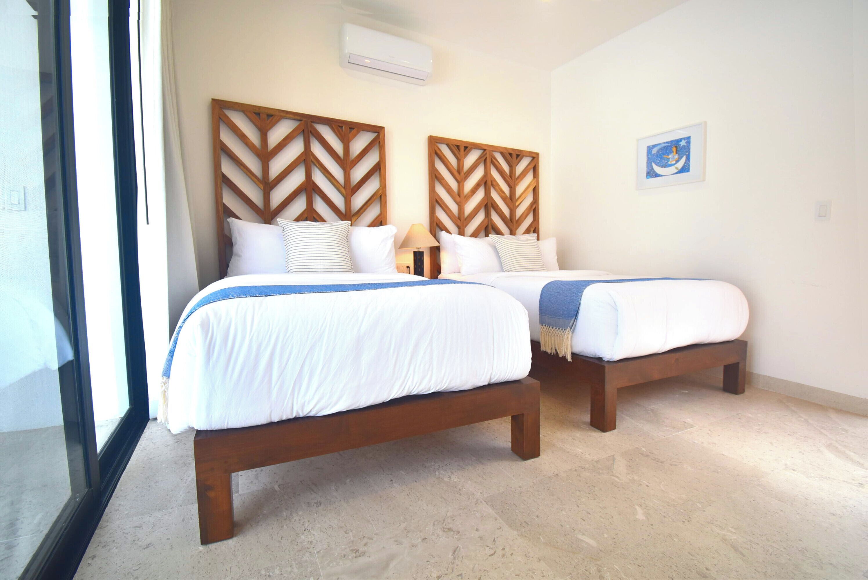 Una habitación de hotel con dos camas, un ventanal grande y un aire acondicionado de pared.