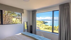 Een slaapkamer met een groot raam dat uitzicht biedt op een meer en begroeiing.