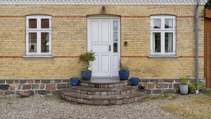A brick building with a white door, two windows, and a small porch with potted plants. - Margretehøj Manor in scenic surroundings (Grenaa)