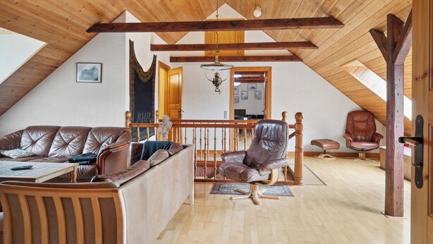 A spacious loft with a high ceiling, wooden beams, a leather sofa, a leather armchair, and a dining area. - Margretehøj Manor in scenic surroundings (Grenaa)