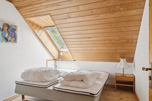 Ein Schlafzimmer mit schrägverdeckter Decke, einem Bett mit weißer Bettwäsche, einem Nachttisch mit Lampe und einem Bild an der Wand.