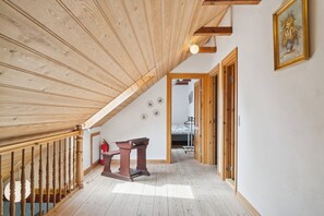 Ein Holzinnenraum mit schrägem Dach, einer Treppe und einem Bett im Hintergrund.