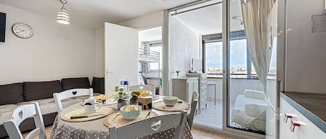 A dining area with a round table, chairs, and a view of the city through a large window.