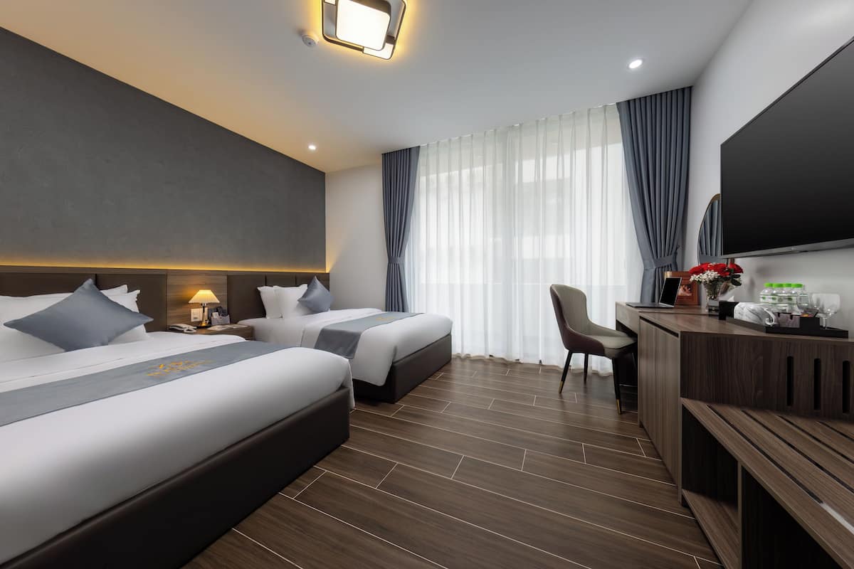A modern hotel room with two beds, a desk, a chair, a TV, and a large window with curtains.