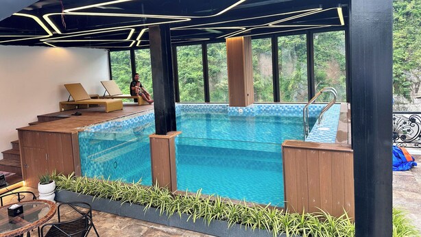 A modern indoor pool area with clear blue water, wooden deck, and lounge chairs. - Cat Ba Wistaria Hotel - Pool & Massage (Hai Phong)