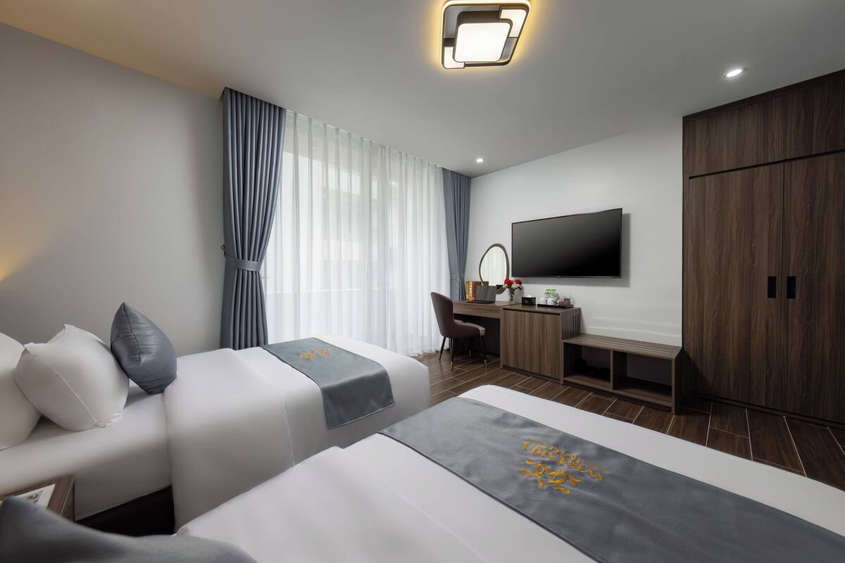A modern hotel room with a sofa, two beds, a desk, a TV, and a wardrobe.