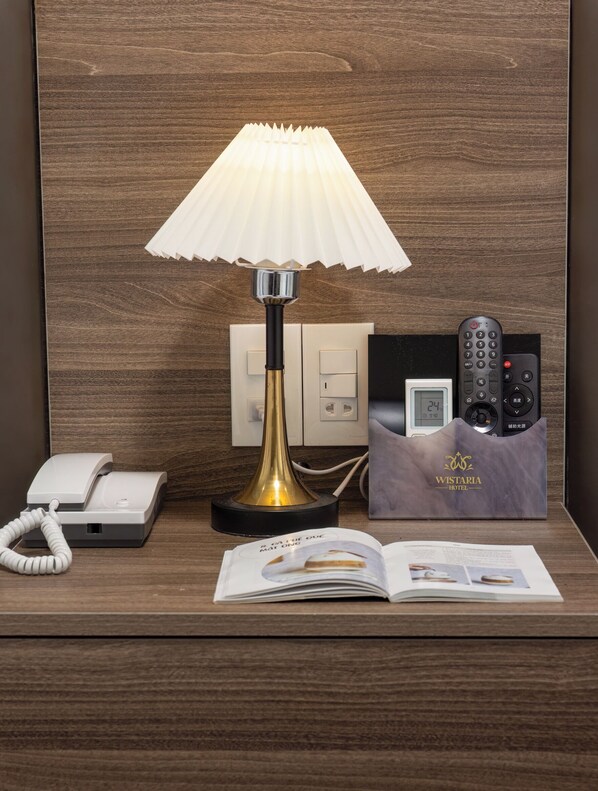 A hotel room with a bedside lamp, a telephone, a remote control, and a brochure on the nightstand. - Cat Ba Wistaria Hotel - Pool & Massage (Hai Phong)