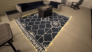 Une terrasse agrémentée d’un tapis à motifs, de meubles d’extérieur et de guirlandes lumineuses.