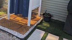 Un patio abrité avec une terrasse en bois, une pergola blanche et une fenêtre donnant sur les arbres.