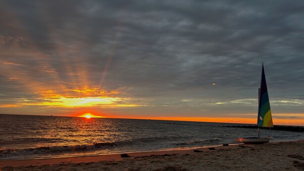 Une scène de plage avec un voilier et un coucher de soleil sur l’océan.