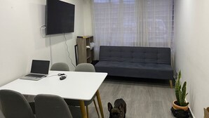 Een moderne woonkamer met een bank, een aan de muur bevestigde televisie, een tafel met een laptop, en een hond.