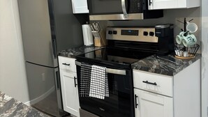 A compact kitchen with white cabinets, a stainless steel refrigerator, a microwave, an oven, and a coffee maker. - New apartment on Main Street in Mackay (Mackay)