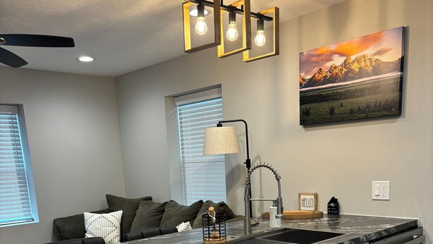 A modern kitchen with a granite countertop, white cabinetry, and a stainless steel sink. There is a trash can, a ceiling fan, and a painting on the wall. - New apartment on Main Street in Mackay (Mackay)