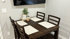 A dining area with a dark wooden table, four chairs, a television mounted on the wall, and a small plant on the table. - New apartment on Main Street in Mackay (Mackay)