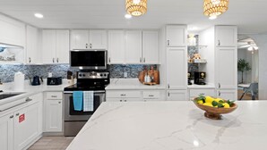 A modern kitchen with white cabinetry, a marble island, and a bowl of lemons.