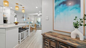 A modern kitchen with white cabinetry, a central island with stools, pendant lighting, and a large abstract painting on the wall.