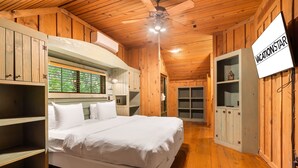 Ein Zimmer in einer Holzhütte mit Bett, fest eingebauten Regalen, einem Fernseher und einem Fenster mit Blick.