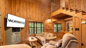 Ein gemütliches Blockhaus-Interieur mit Holzwänden, einem an einem Schrank befestigten Fernseher und einer Treppe, die zu einer oberen Ebene führt.