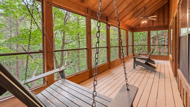 Eine Holzterrasse mit Schaukelbänken und Deckenventilator, mit Blick auf ein bewaldetes Gebiet.