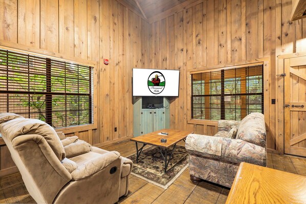 A cozy room with wooden walls, a TV mounted on the wall, a sofa, a recliner, and a coffee table.