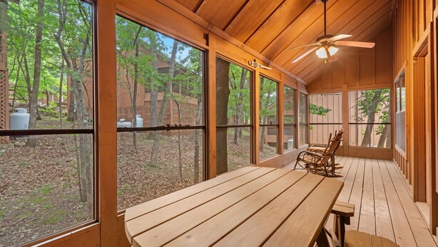 Una terraza de madera con una mesa, sillas, ventanas amplias y un ventilador de techo.