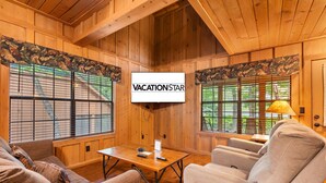 Una habitación acogedora con paredes de madera, una pantalla de televisión grande, una mesa de madera y asientos cómodos.
