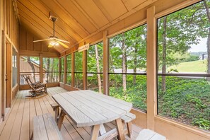 A wooden deck with a picnic table and chairs, large windows offering a view of the surrounding greenery.