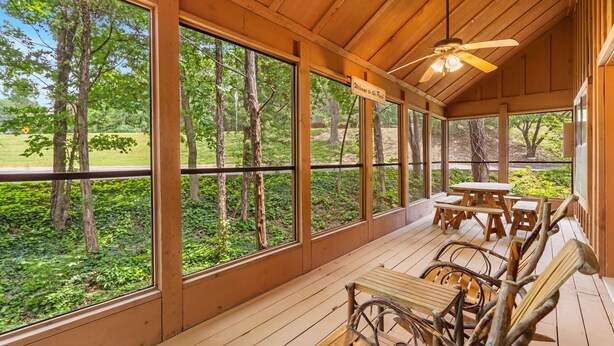 Una terraza de madera con ventanas amplias, ventilador de techo y mesas de picnic.