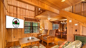 A wooden interior with a dining area, a sofa, and a TV displaying a logo. - Branson Cabin Near Attractions, Dining & Shows (Branson)