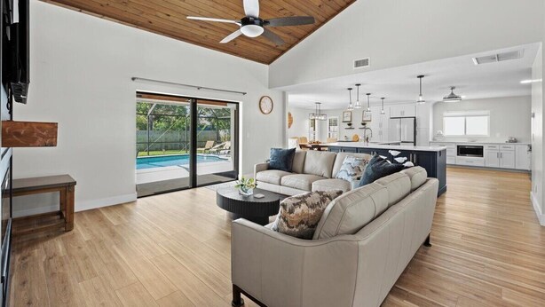 Un salon spacieux avec un grand canapé, une table basse et un ventilateur de plafond. Une porte-fenêtre coulissante donne accès à une zone avec piscine.