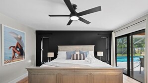 Une chambre avec un grand lit, un ventilateur de plafond et une vue sur une piscine.