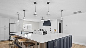Une cuisine moderne dotée d’un grand îlot central, de tabourets de bar et de luminaires suspendus.