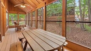 Una terraza de madera con una mesa, sillas, ventanas amplias y un ventilador de techo.