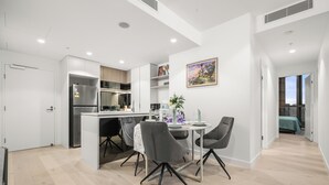 A modern kitchen with white cabinetry, a built-in island, and a dining area with a table and chairs.