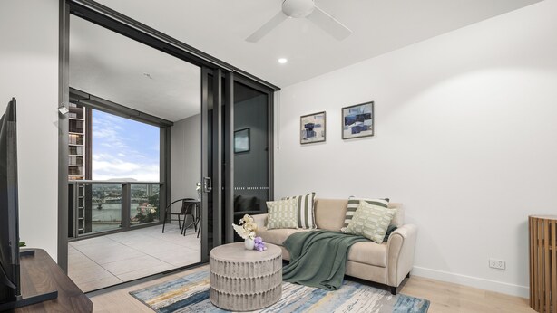 A modern living room with a sofa, a coffee table, and a view of a cityscape through large windows.