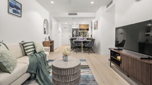 A modern living room with a sofa, coffee table, TV stand, and dining area.