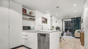A modern kitchen with a dishwasher, a microwave, and a sink. There is a dining area with a chair and a table.