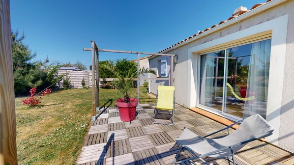 A patio with wooden decking, a yellow chair, a red potted plant, and a white chair.
